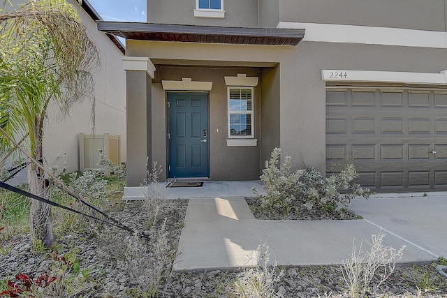 view of exterior entry with a garage and stucco siding