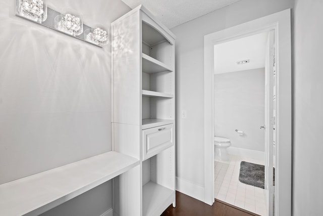 interior space featuring a textured ceiling, baseboards, toilet, and tile patterned floors