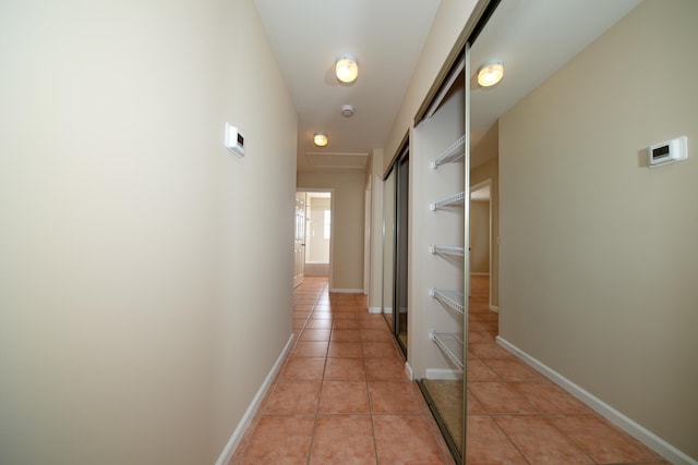 hall with light tile patterned floors, baseboards, and attic access