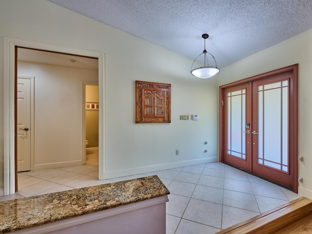 entrance foyer with a textured ceiling, french doors, light tile patterned flooring, and baseboards