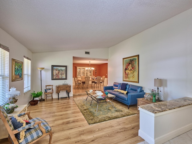 living area featuring lofted ceiling, a textured ceiling, visible vents, light wood-style floors, and an inviting chandelier