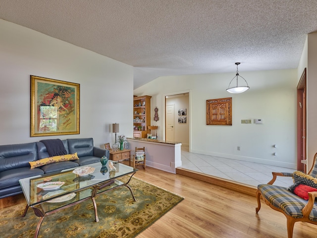 living room featuring vaulted ceiling, a textured ceiling, baseboards, and light wood-style floors