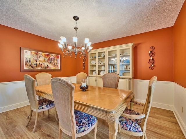 dining area with light wood-type flooring, wainscoting, a textured ceiling, and an inviting chandelier