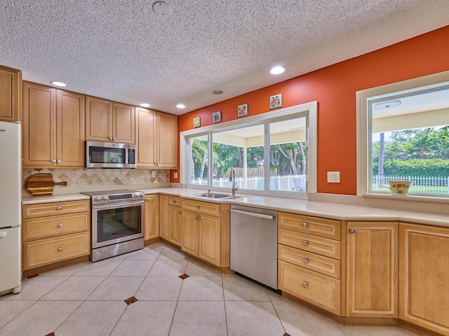 kitchen featuring tasteful backsplash, stainless steel appliances, light countertops, a sink, and light tile patterned flooring