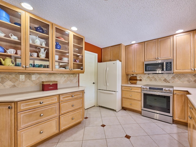 kitchen with stainless steel appliances, light countertops, glass insert cabinets, and light tile patterned floors