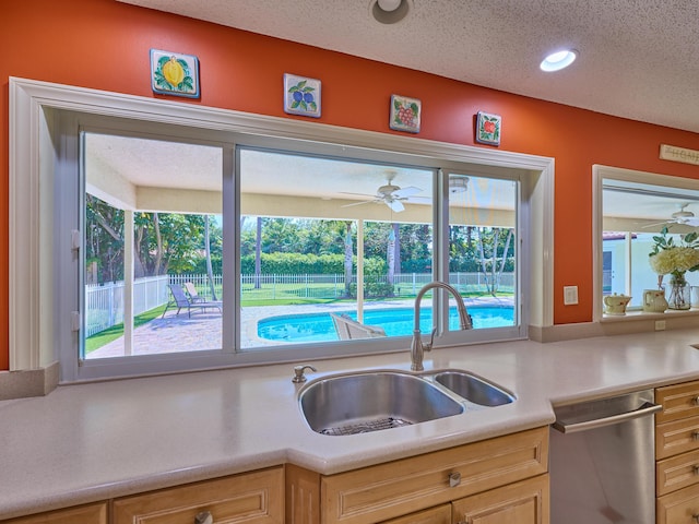 kitchen featuring a textured ceiling, a sink, light countertops, stainless steel dishwasher, and light brown cabinetry