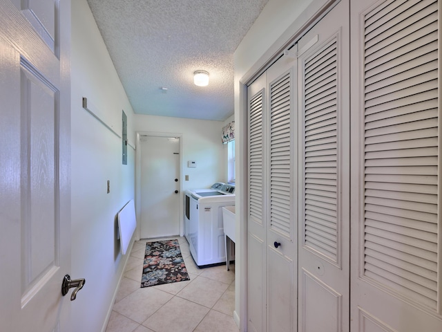 laundry area featuring light tile patterned floors, a textured ceiling, washing machine and dryer, laundry area, and baseboards