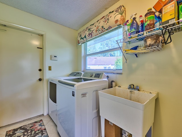 washroom with a textured ceiling, light tile patterned flooring, laundry area, a sink, and washing machine and clothes dryer