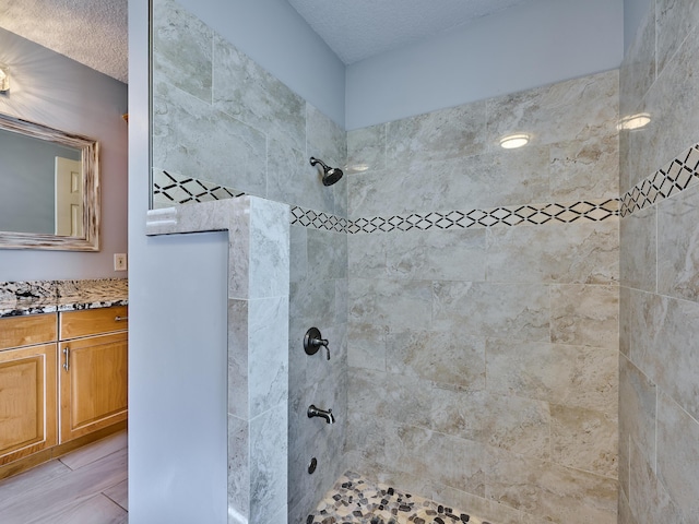 bathroom featuring a tile shower, vanity, and a textured ceiling