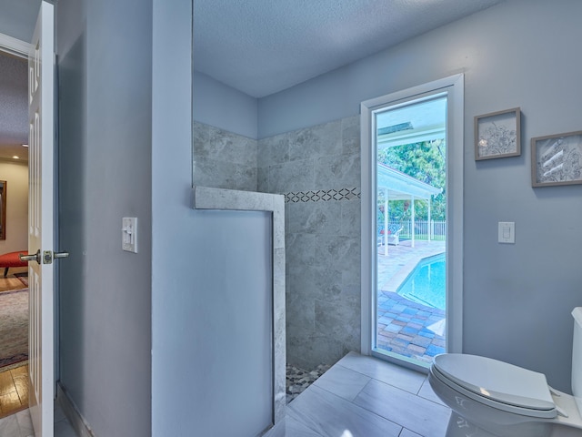 full bathroom with toilet, a shower, a textured ceiling, and tile patterned floors