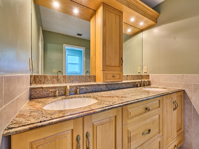 bathroom featuring visible vents, a sink, tile walls, and double vanity