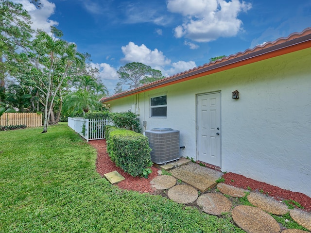 exterior space featuring a tile roof, a yard, stucco siding, central air condition unit, and fence