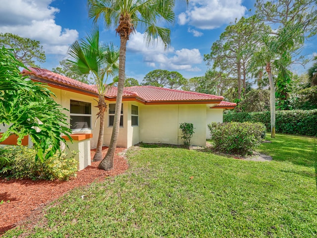 exterior space featuring a tile roof, a lawn, and stucco siding