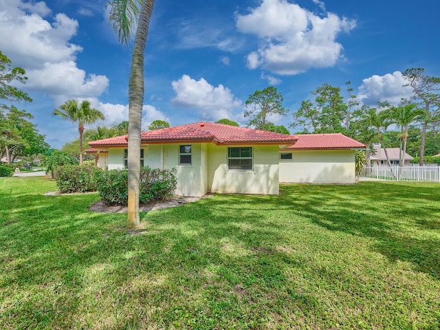 rear view of house featuring fence, a lawn, and a tiled roof