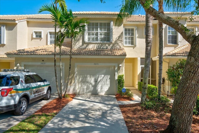 townhome / multi-family property with an attached garage, driveway, a tiled roof, and stucco siding