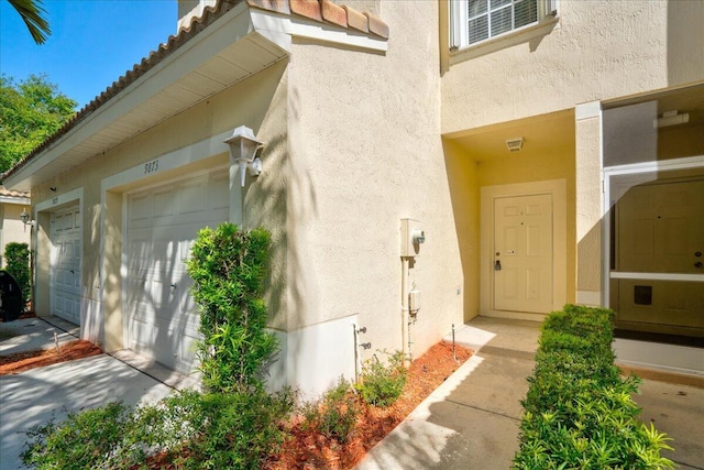 entrance to property with a garage, a tiled roof, and stucco siding