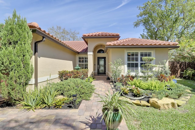 mediterranean / spanish house with fence, a tile roof, and stucco siding