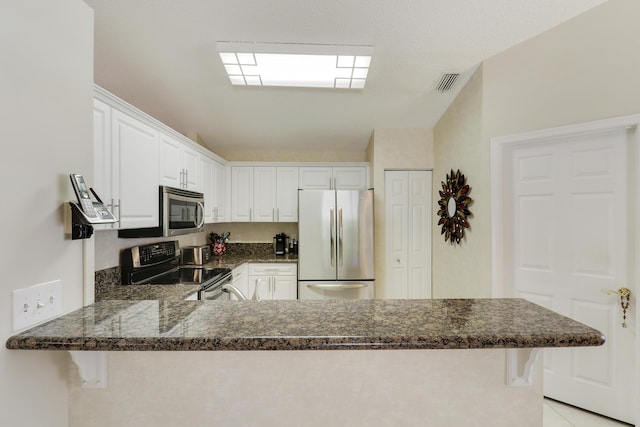 kitchen with a breakfast bar area, a peninsula, visible vents, white cabinetry, and appliances with stainless steel finishes