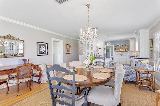 dining space featuring visible vents, ornamental molding, light wood-style flooring, and an inviting chandelier