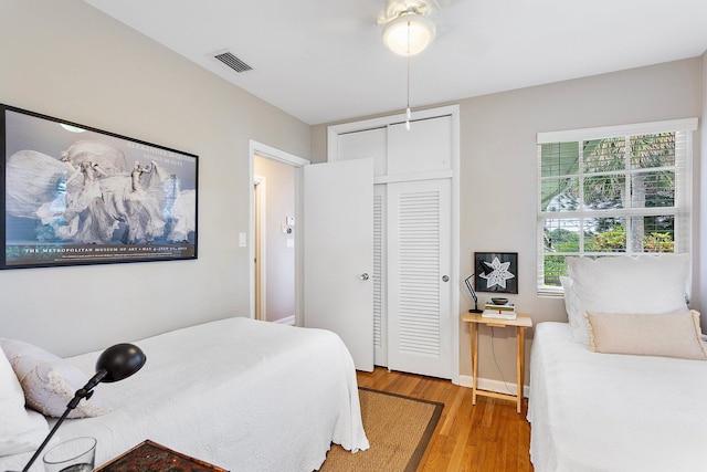 bedroom with a closet, wood finished floors, visible vents, and baseboards