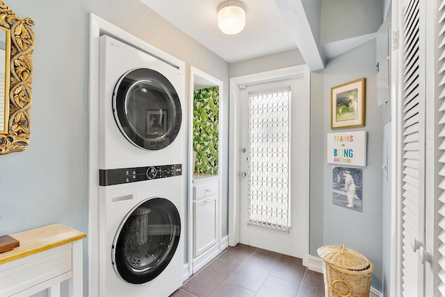 laundry area with a healthy amount of sunlight, dark tile patterned flooring, and stacked washer and clothes dryer