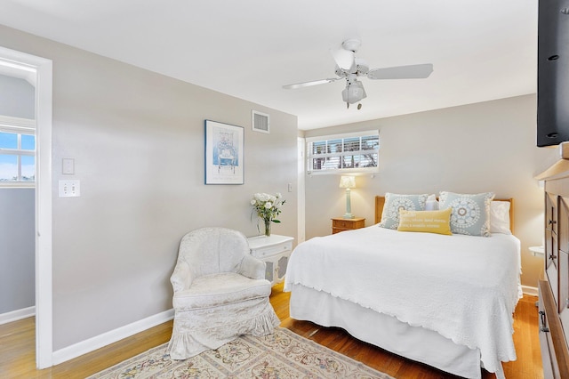 bedroom featuring baseboards, multiple windows, visible vents, and wood finished floors