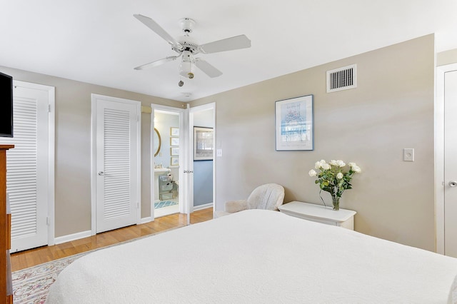 bedroom with visible vents, baseboards, ensuite bath, wood finished floors, and two closets