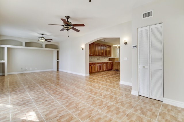 unfurnished living room with arched walkways, visible vents, a ceiling fan, light tile patterned flooring, and baseboards