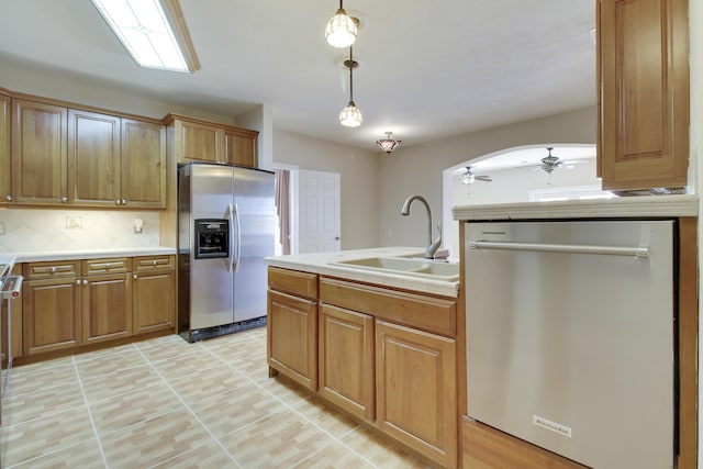 kitchen with arched walkways, stainless steel appliances, a sink, tasteful backsplash, and brown cabinetry