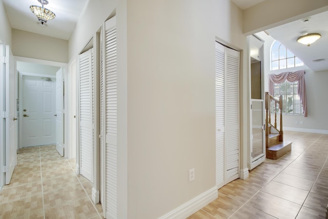 corridor featuring stairs, light tile patterned flooring, visible vents, and baseboards