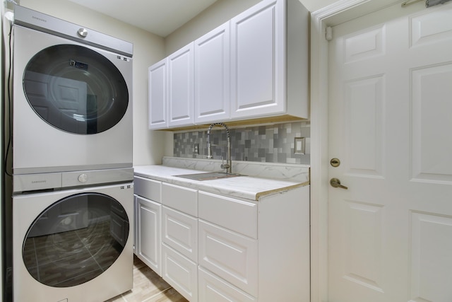 laundry room featuring cabinet space, a sink, and stacked washer and clothes dryer