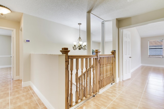 hallway featuring light tile patterned floors, a chandelier, a textured ceiling, and an upstairs landing