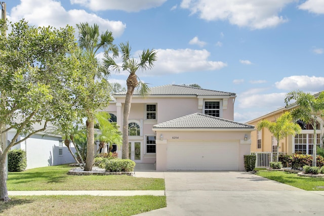 mediterranean / spanish-style house with an attached garage, a tiled roof, concrete driveway, stucco siding, and a front yard