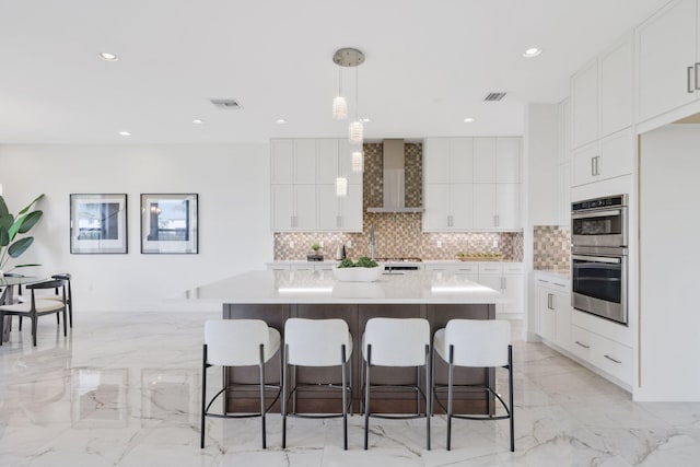 kitchen featuring a breakfast bar area, stainless steel double oven, visible vents, backsplash, and wall chimney exhaust hood