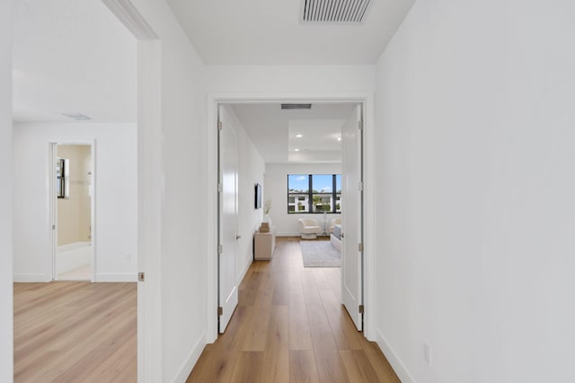 hall featuring light wood-type flooring, visible vents, and baseboards