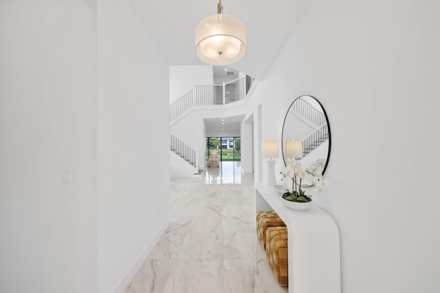 hall with a towering ceiling, marble finish floor, stairway, and baseboards