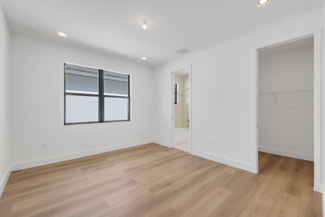 unfurnished bedroom with light wood-style flooring, a spacious closet, baseboards, and recessed lighting