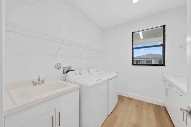 washroom featuring a sink, baseboards, light wood-type flooring, independent washer and dryer, and cabinet space