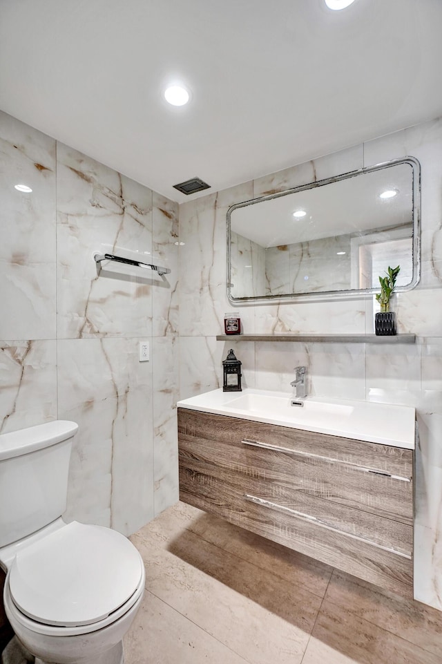 bathroom featuring a marble finish shower, visible vents, toilet, vanity, and tile walls