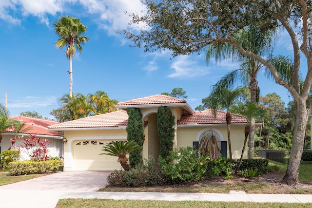 mediterranean / spanish-style house featuring driveway, a tiled roof, an attached garage, fence, and stucco siding