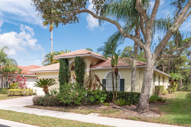 view of front of property with decorative driveway, stucco siding, a garage, a tiled roof, and a front lawn