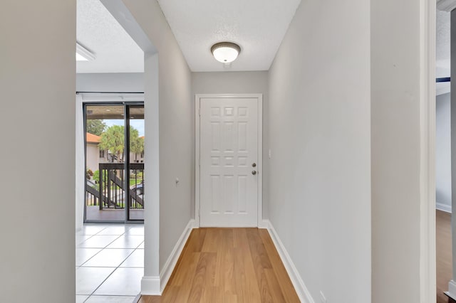 doorway featuring light wood-type flooring, a textured ceiling, and baseboards