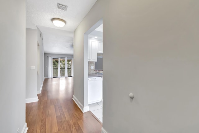 corridor featuring baseboards, visible vents, a textured ceiling, and light wood finished floors