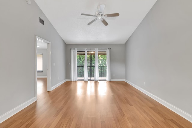 empty room with light wood finished floors, visible vents, a ceiling fan, vaulted ceiling, and baseboards