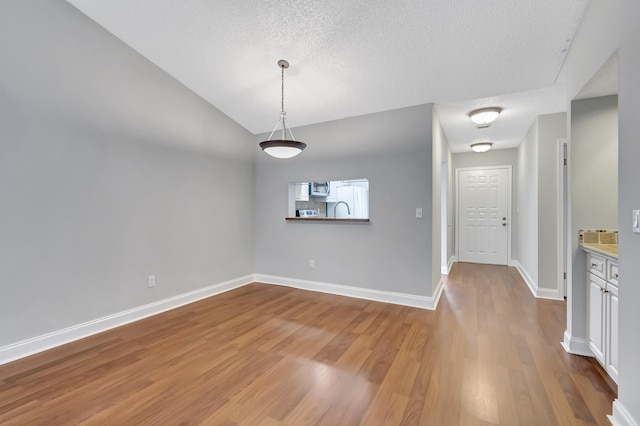 unfurnished dining area with a textured ceiling, vaulted ceiling, wood finished floors, and baseboards