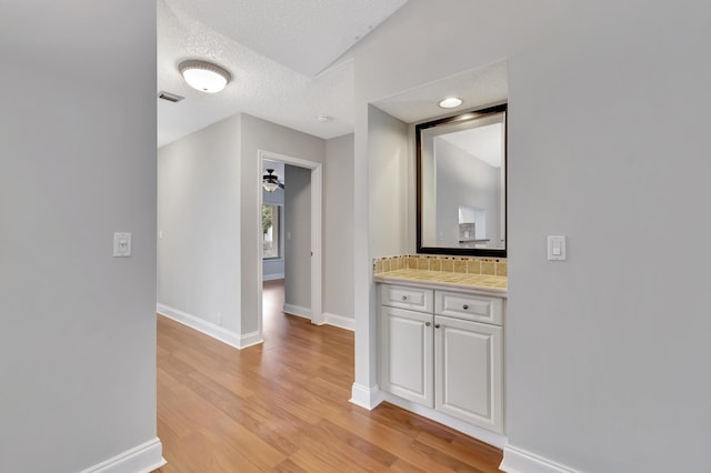 hallway with light wood finished floors, visible vents, baseboards, and a textured ceiling