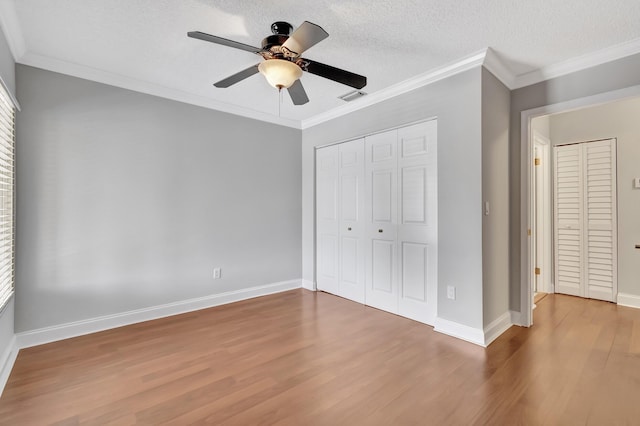 unfurnished bedroom with a textured ceiling, visible vents, wood finished floors, and ornamental molding