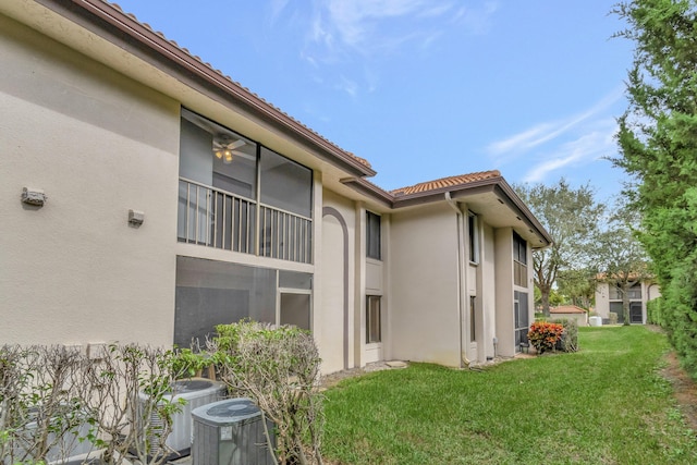 view of side of home with stucco siding, a tiled roof, central AC, and a yard