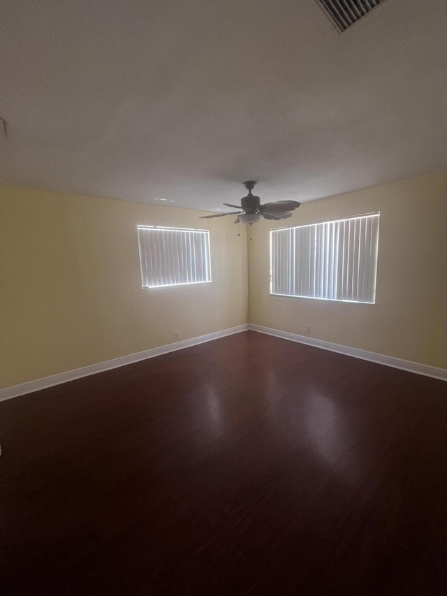 spare room with visible vents, dark wood finished floors, a ceiling fan, and baseboards