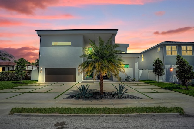 contemporary house featuring a garage, concrete driveway, fence, and stucco siding